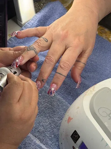 Nail technician detailing nail art with an electric file